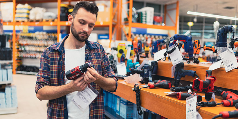Man stands in front of a wall of power tools inspecting a drill