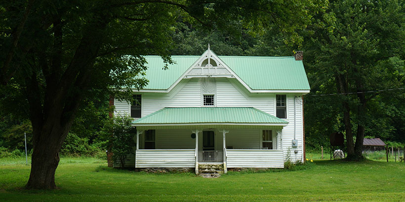 Rural green and white home flanked by old growth trees