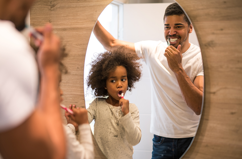 Father and son brush teeth together in a bathroom mirror