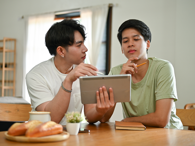 Couple sitting at kitchen table with a tablet and notepad