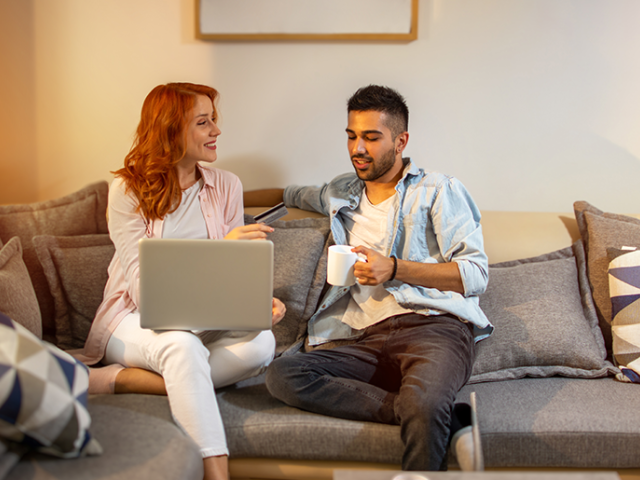 Man and woman share a couch to review their shared finances on a laptop