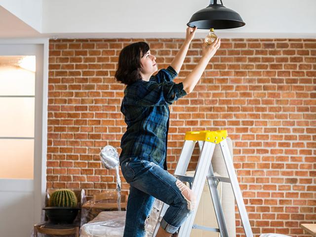 Handy woman changes lightbulb while standing on a ladder