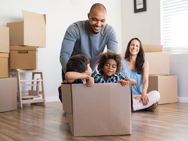 Two kids sitting in a box as parents unpack from a move