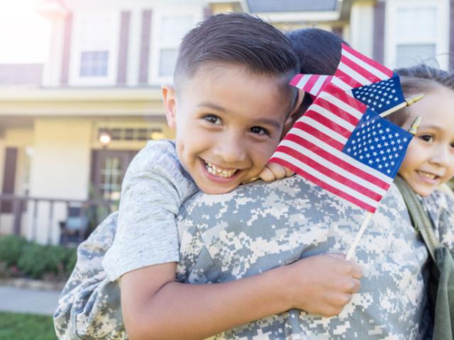 Image of soldier hugging small children holding American flags