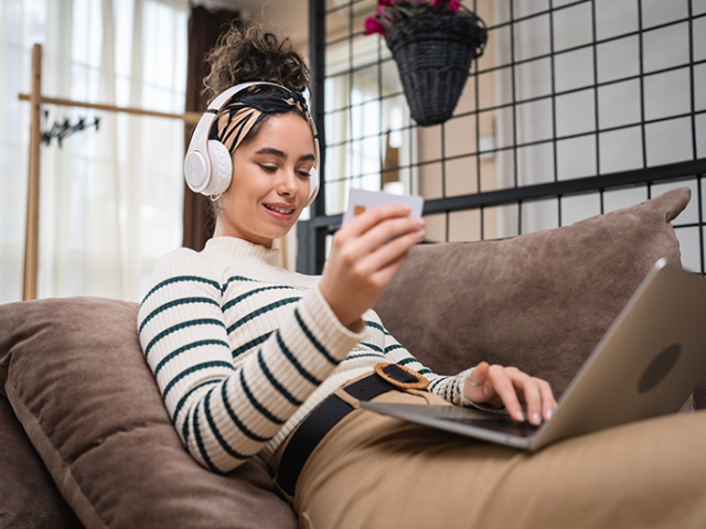 Woman online shopping on the couch entering credit card info with headphones on