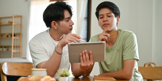 Couple sitting at kitchen table with a tablet and notepad