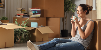 Woman sitting on floor with coffee surrounded by boxes