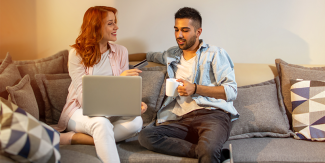 Man and woman share a couch to review their shared finances on a laptop