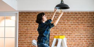 Handy woman changes lightbulb while standing on a ladder