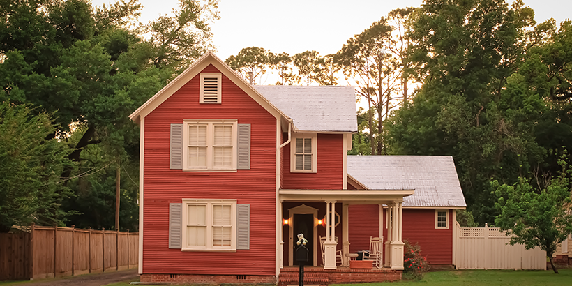 Red house with white fence surrounded by trees