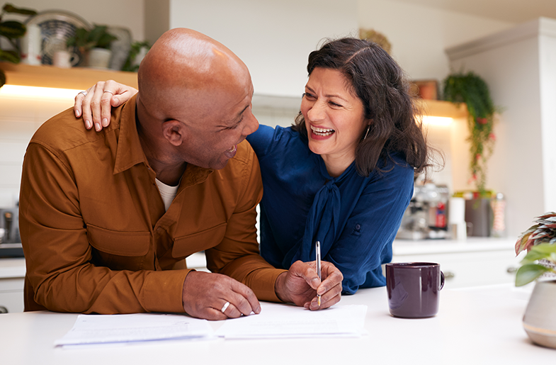 Husband and wife hugging while he signs a document at the kitchen counter