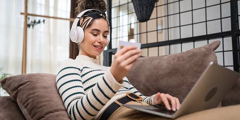 Woman online shopping on the couch entering credit card info with headphones on