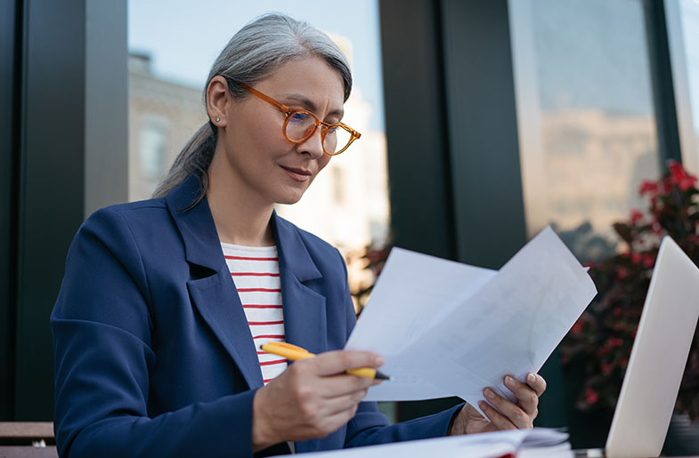 Gray-haired woman analyzing important reports.