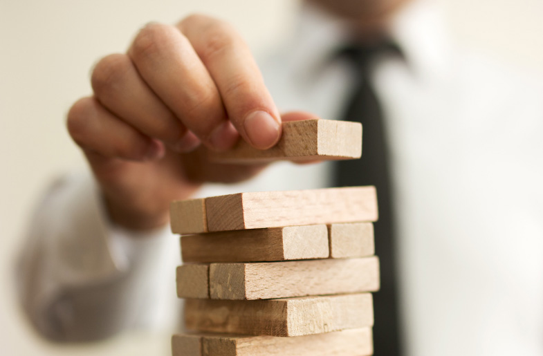 A hand reaches out with a wooden block to add to the top of the Jenga game