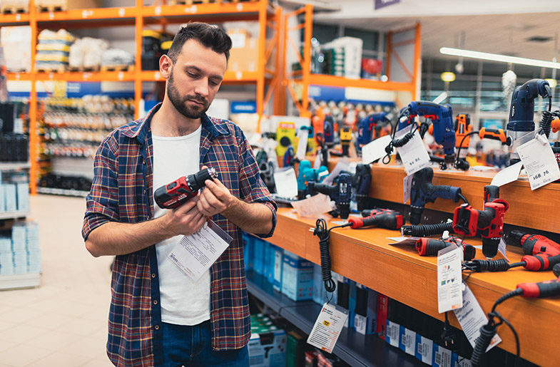 Man stands in front of a wall of power tools inspecting a drill
