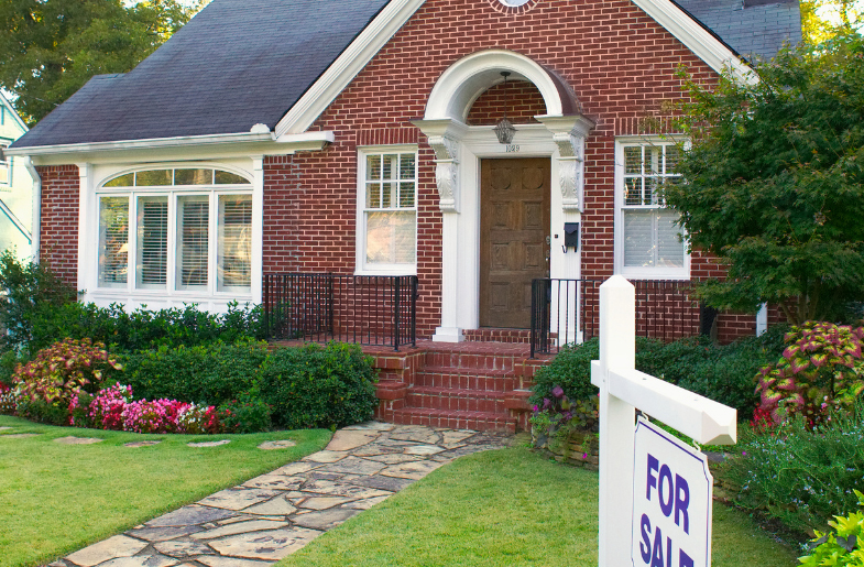 small red brick home that has a for sale sign 