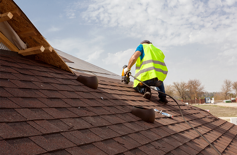 Roofer installing roof shingles with power tools.
