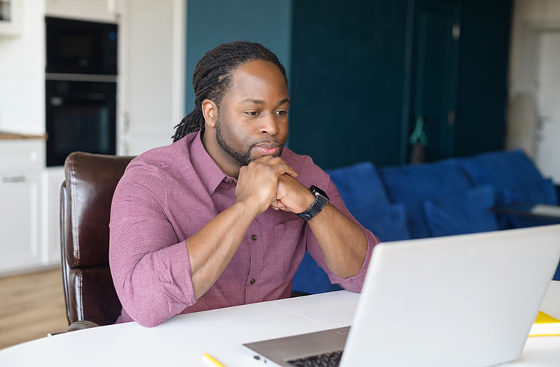 Young man siting at a disk looking at laptop.