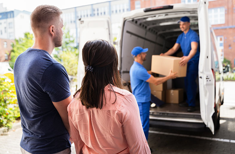 Man and woman watch movers load moving-boxes into moving truck.