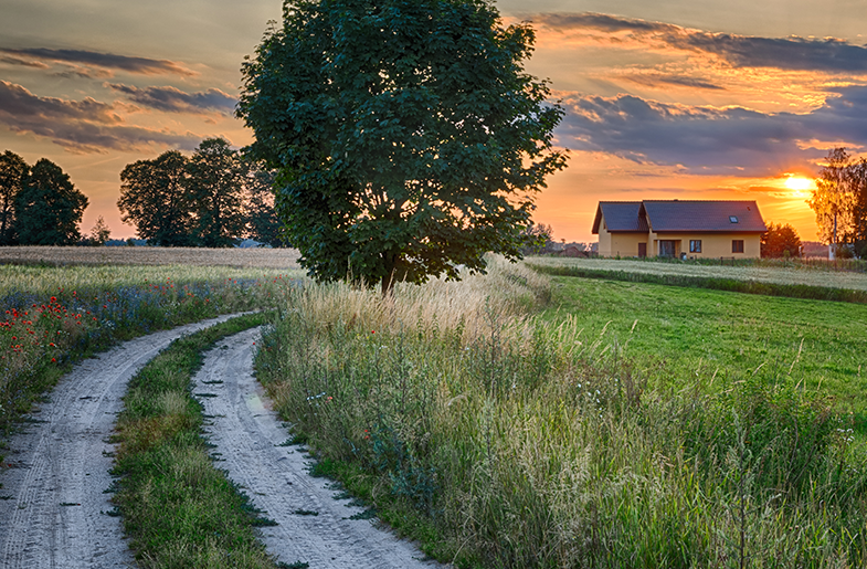 Sun setting behind a house on a rural road