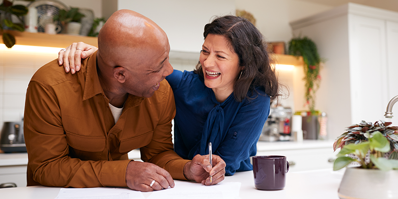 Husband and wife hugging while he signs a document at the kitchen counter