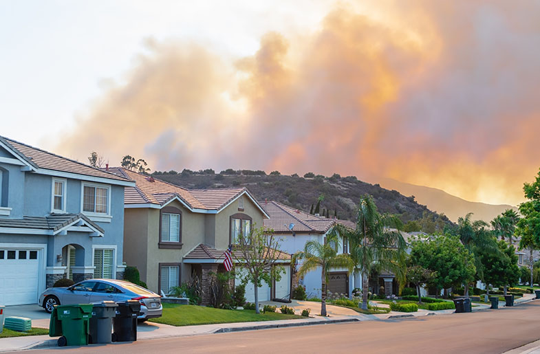 Visible wildfire smoke in the mountain landscape behind houses.