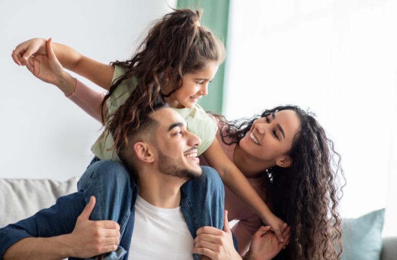 Father carries young daughter on his shoulders, while the girl and mother look at each other, smiling