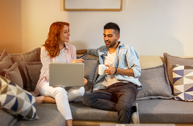 Man and woman share a couch to review their shared finances on a laptop