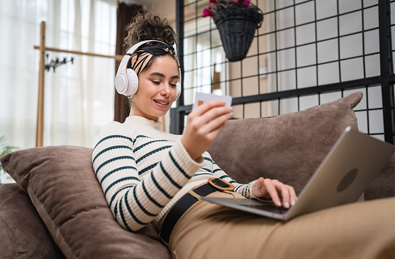 Woman online shopping on the couch entering credit card info with headphones on